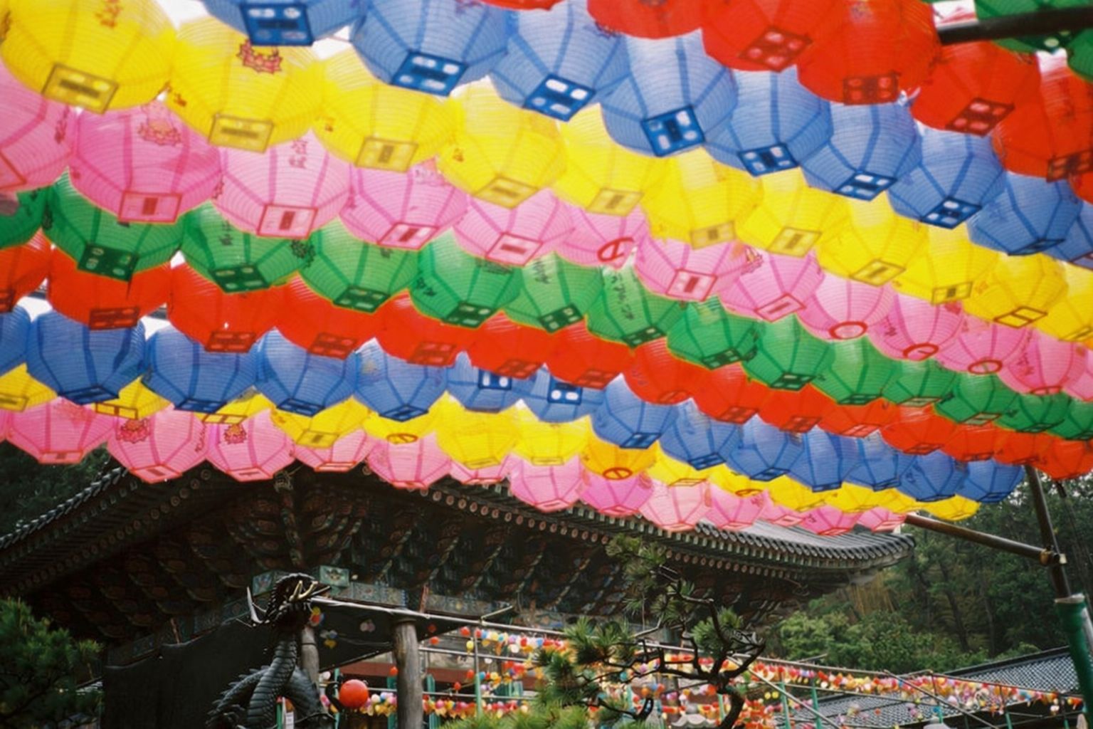 Färgglada lyktor i rader ovanför ett tempeltak, som en festlig installation.